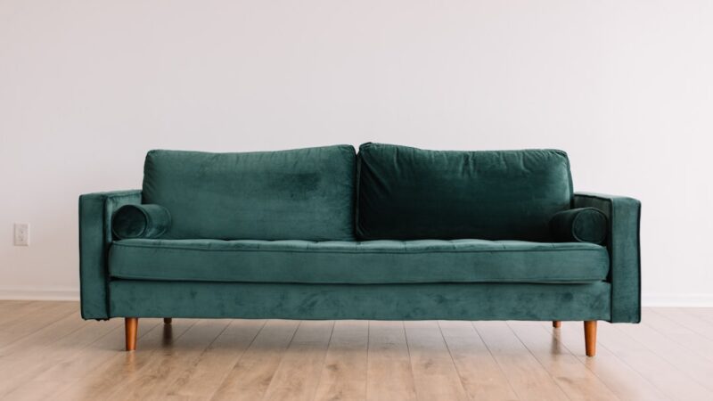 Cool hipster green couch sofa with brown wooden legs on wooden floor